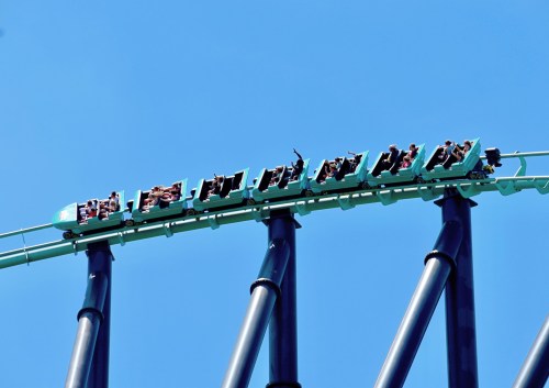 A roller coaster car with riders at the peak of a loop against a clear blue sky.