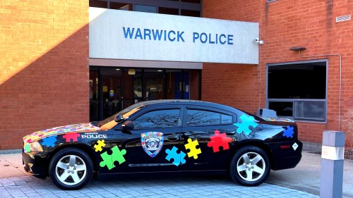 A decorated police car with colorful puzzle pieces parked outside the Warwick Police station.