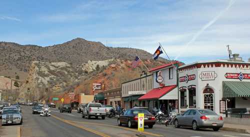 A quaint street scene with shops, flags, and mountains in the background, showcasing a small-town atmosphere.