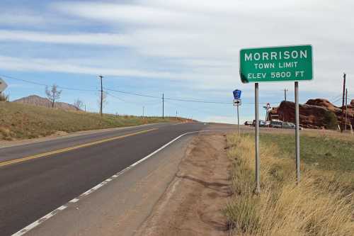 Sign marking the town limit of Morrison, elevation 5800 ft, alongside a winding road with grassy shoulders.