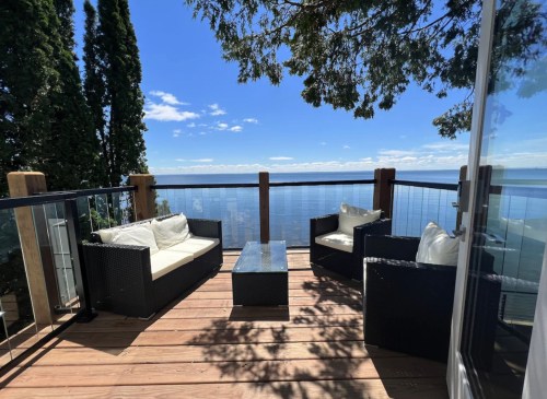 A cozy outdoor seating area with two chairs and a table, overlooking a serene lake and blue sky.