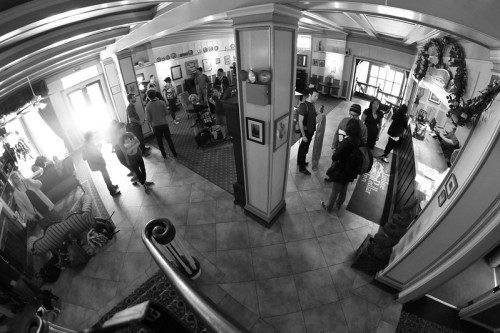 A spacious hotel lobby filled with people, featuring a mix of seating areas and decorative elements in black and white.