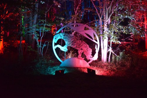 A illuminated metal sculpture of a panther surrounded by colorful lights in a forest setting.