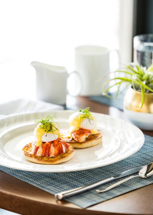 Two eggs Benedict on toasted English muffins, topped with salmon and garnished with dill, served on a white plate.
