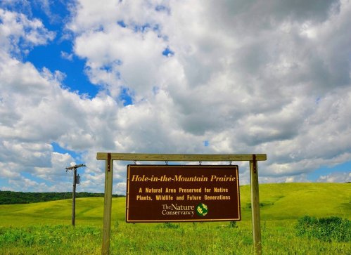 Sign for Hole-in-the-Mountain Prairie, a nature preserve for native plants and wildlife, set against a blue sky.
