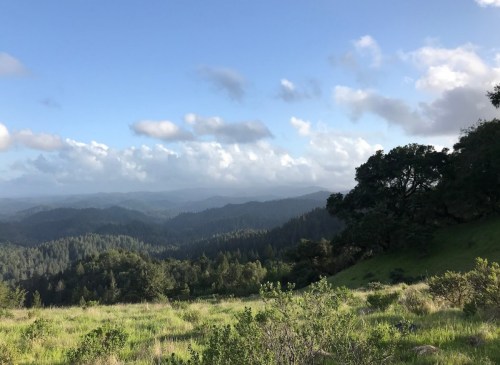 A scenic view of rolling green hills and mountains under a partly cloudy sky.