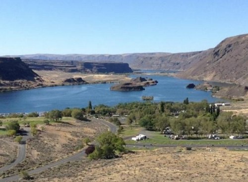 A scenic view of a river winding through rocky hills, with green trees and a campground in the foreground.