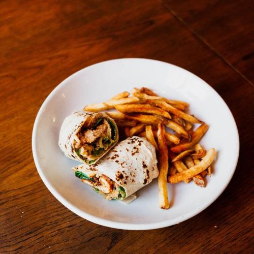 A plate with a chicken wrap and a side of golden French fries on a wooden table.