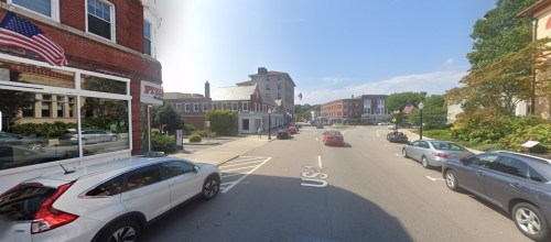 A street view showing parked cars, buildings, and an American flag on a clear day.