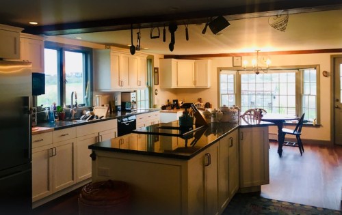 Bright kitchen with white cabinets, a large island, and a dining area with a table and chairs by a window.