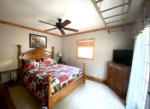 Cozy bedroom with a wooden bed, patterned bedding, a ceiling fan, and a small TV in a wooden cabinet.