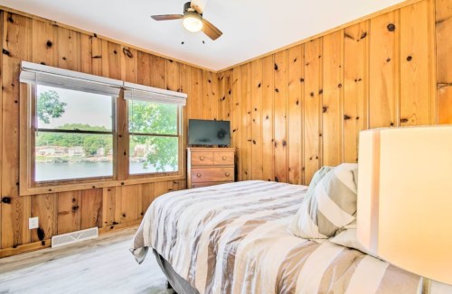 Cozy bedroom with wooden walls, a bed, lamp, and window overlooking a lake view.