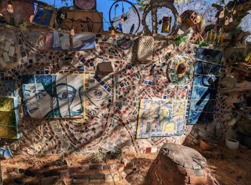 Colorful mosaic wall featuring various artistic portraits and designs, surrounded by natural elements and hanging lights.