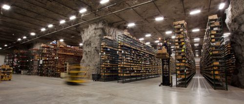 A large underground warehouse with tall shelves filled with boxes and a forklift in motion.