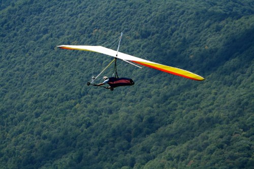 A hang glider soaring over a lush green mountain landscape on a clear day.