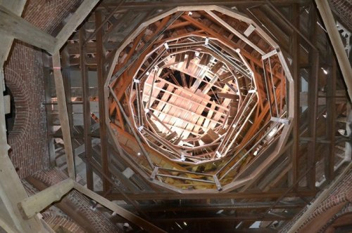 View looking up through a spiral wooden structure with exposed beams and brick walls.