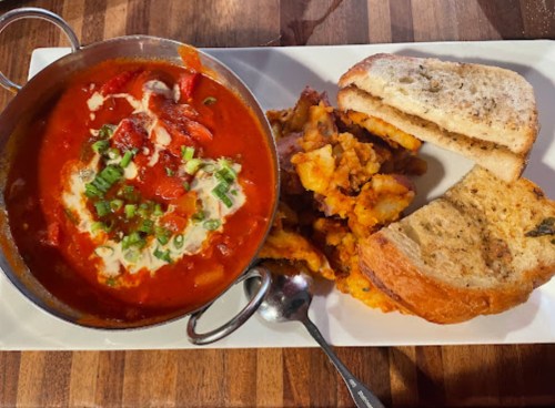 A bowl of tomato soup with herbs, served with crispy potatoes and slices of toasted bread on a white plate.