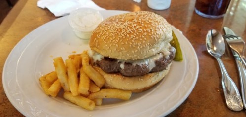 A sesame seed bun burger with melted cheese, served with a side of French fries and a pickle on a white plate.