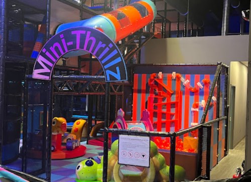 Colorful indoor play area with slides, climbing structures, and soft toys, labeled "Mini-Thrillz."