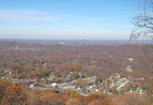 A panoramic view of a valley with autumn foliage, featuring small towns and rolling hills under a clear blue sky.