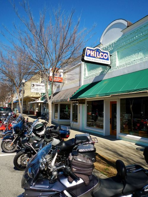 A row of motorcycles parked in front of a storefront with a sign reading "Philco" on a sunny day.
