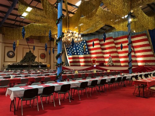 A decorated hall with a large American flag backdrop, festive tables, and holiday decorations for an event.