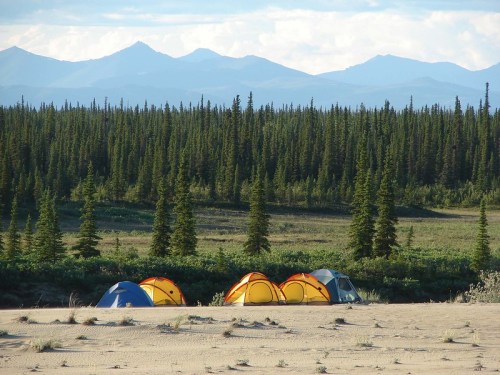 A serene campsite with colorful tents set against a backdrop of mountains and dense evergreen trees.