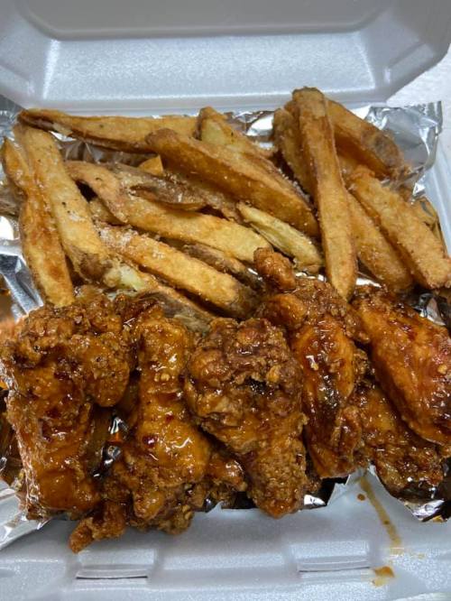 A takeout container filled with crispy fried chicken wings and golden-brown French fries.
