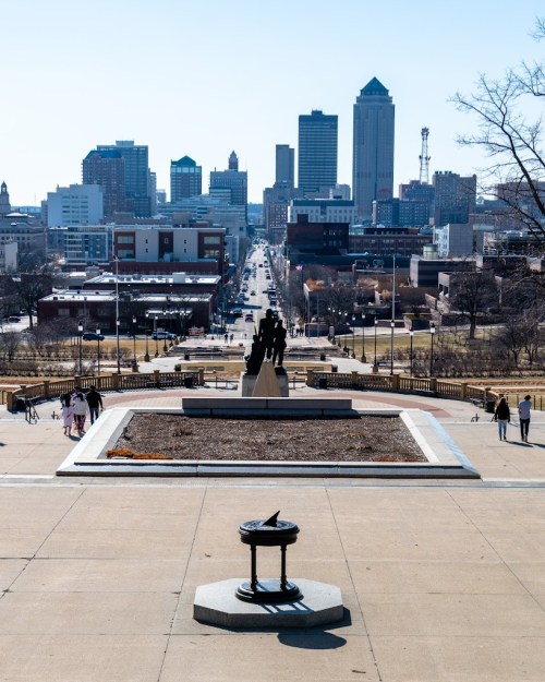 View from a park overlooking a city skyline, with a statue in the foreground and a clear blue sky above.