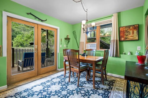 Bright dining area with green walls, wooden table, chairs, and large windows overlooking a deck. Cozy and inviting atmosphere.