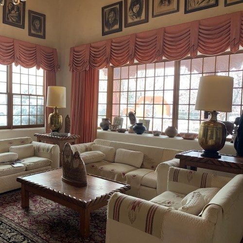 Cozy living room with white sofas, wooden coffee table, decorative lamps, and framed portraits on the walls.