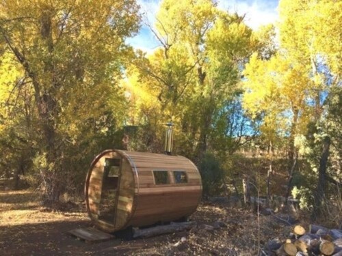 A wooden barrel-shaped cabin surrounded by vibrant yellow trees in a serene outdoor setting.