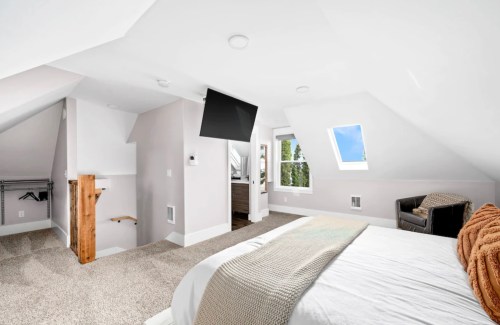 Bright, modern attic bedroom with a sloped ceiling, large window, and cozy furnishings.
