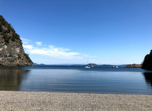 A serene coastal scene with calm waters, boats in the distance, and rocky cliffs under a clear blue sky.