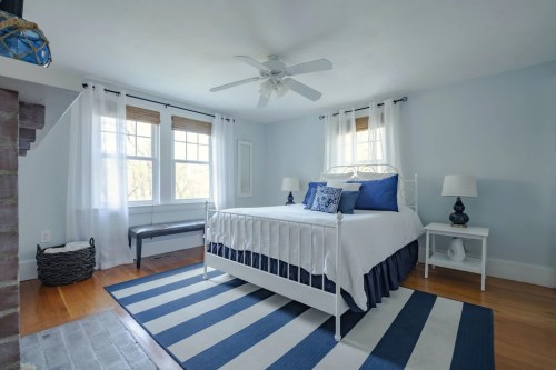 Bright bedroom with a white bed, blue accents, large windows, and a striped rug. Cozy and inviting atmosphere.
