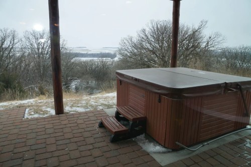 A hot tub on a patio overlooking a snowy landscape with trees in the background.