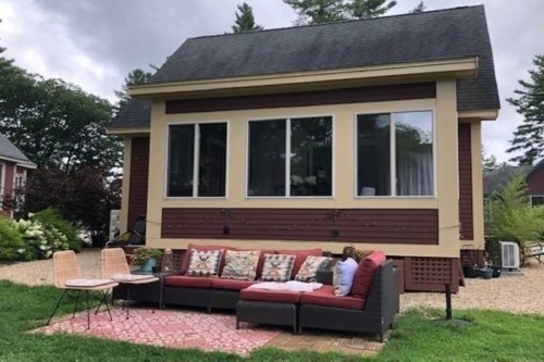 A cozy house with large windows, featuring a red outdoor sofa and two small tables on a gravel patio.