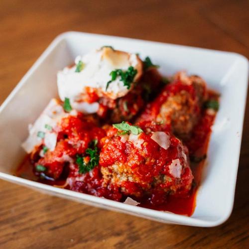 A bowl of meatballs in marinara sauce, garnished with herbs and onions, served on a wooden table.