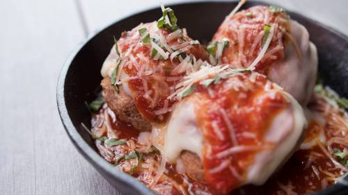 Three meatballs topped with marinara sauce, melted cheese, and fresh basil, served in a cast iron skillet.