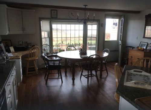 A cozy kitchen with a round table, wooden chairs, and large windows overlooking a scenic view.