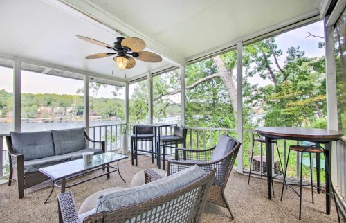 A cozy screened-in porch with seating, a ceiling fan, and a view of trees and water.