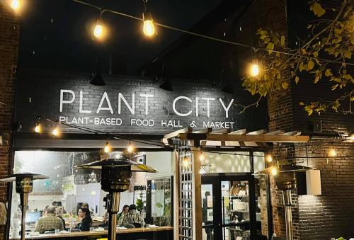 Exterior of Plant City, a plant-based food hall and market, illuminated by string lights at night.