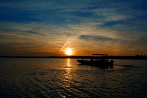 A silhouette of a boat on water at sunset, with vibrant clouds and a golden horizon.