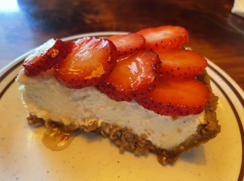 A slice of cheesecake topped with fresh strawberries on a white plate.