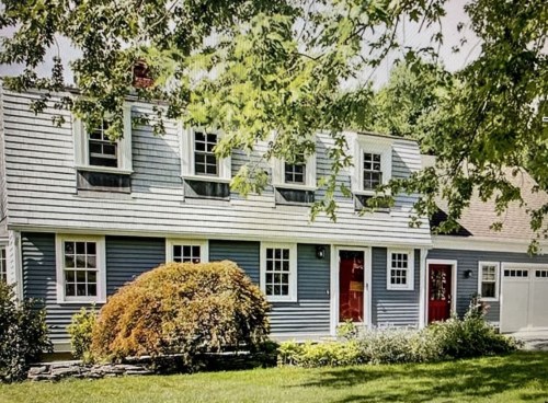 A charming blue house with white trim, red doors, and a well-kept garden, surrounded by trees and greenery.