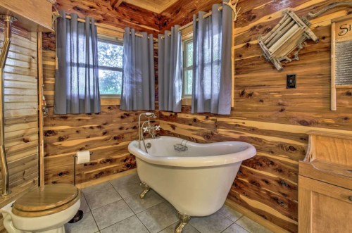 Cozy bathroom featuring a vintage clawfoot tub, wooden walls, and gray curtains by a window.