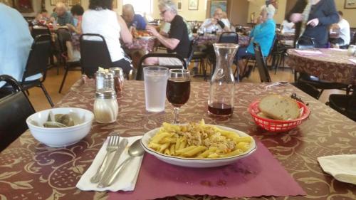 A table set with a plate of pasta, a glass of water, and a carafe, in a busy dining room with people eating.