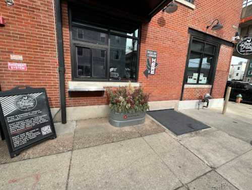 Exterior view of a brick building with a planter, a sign for pickup, and a ramp leading to the entrance.