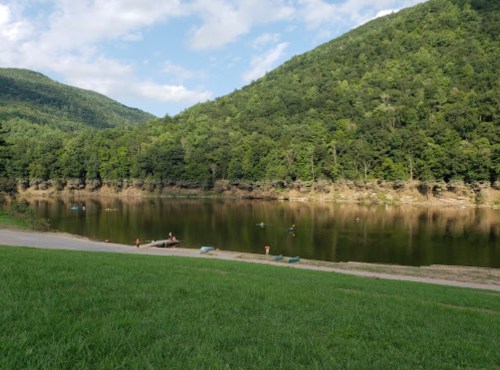 A serene lake surrounded by green hills, with people fishing and enjoying the outdoors on a sunny day.