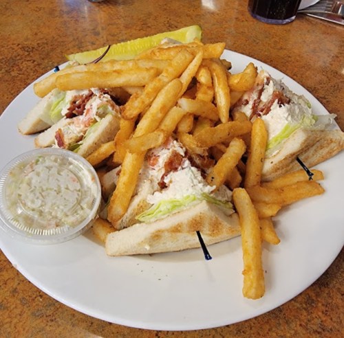 A plate with three sandwich triangles filled with chicken salad, served with fries and a side of coleslaw.